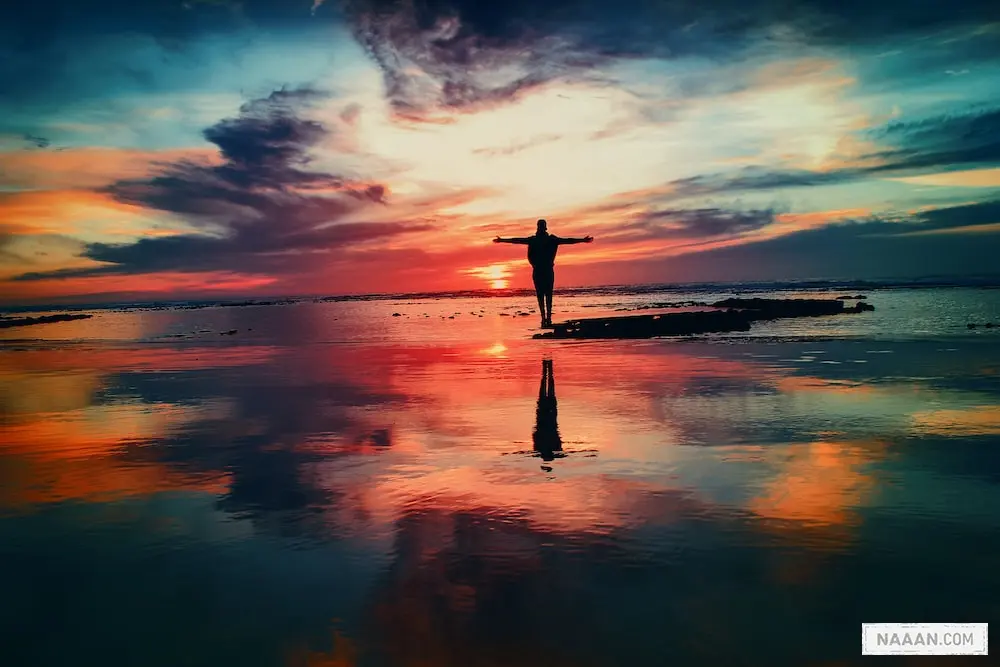 silhouette of person standing on rock surrounded by body of water
