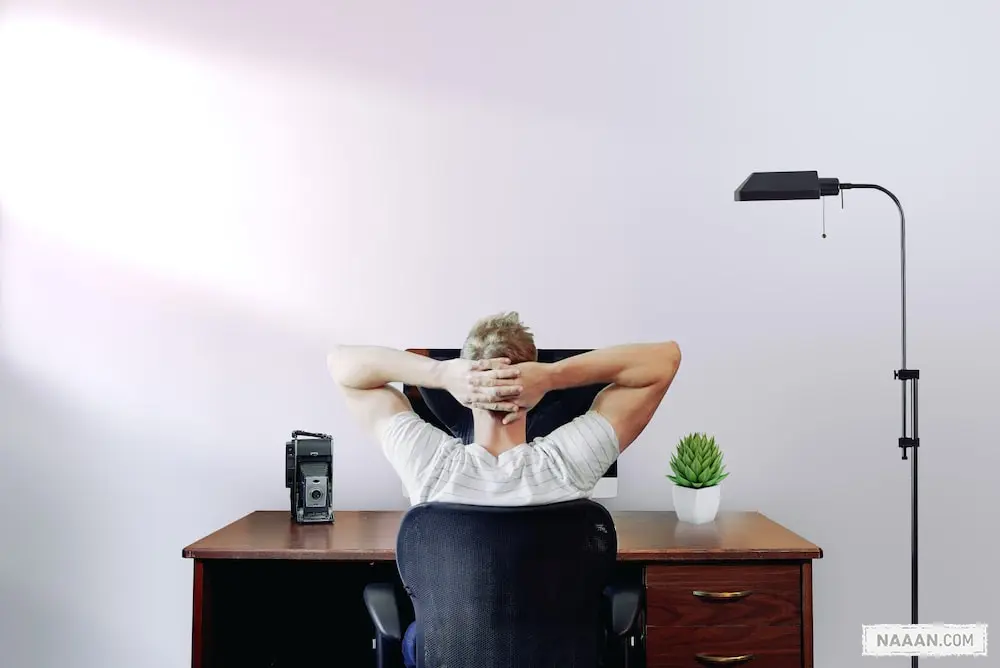 man holding his head while sitting on chair near computer desk